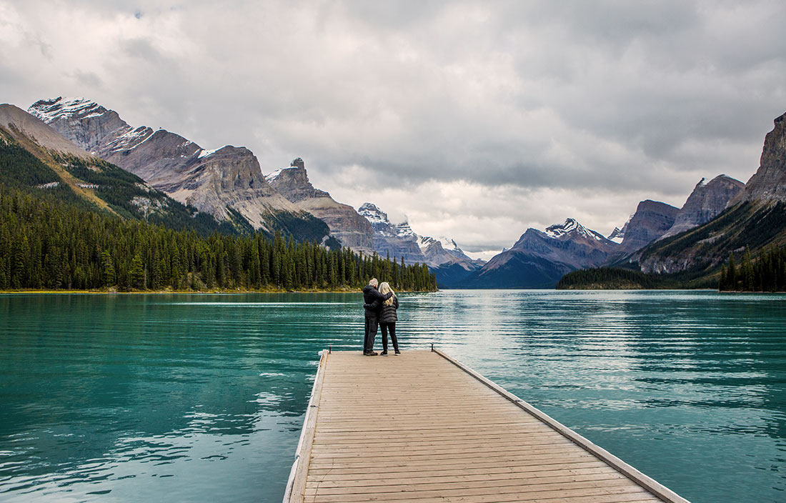 Senior couple at end of a long dock looking out at a lake and mountains in the distance