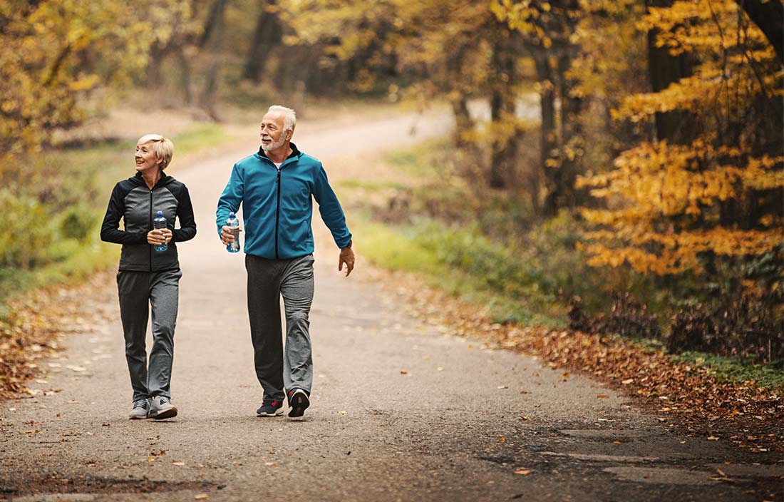 Two active senior adults walking next to a forest in fall