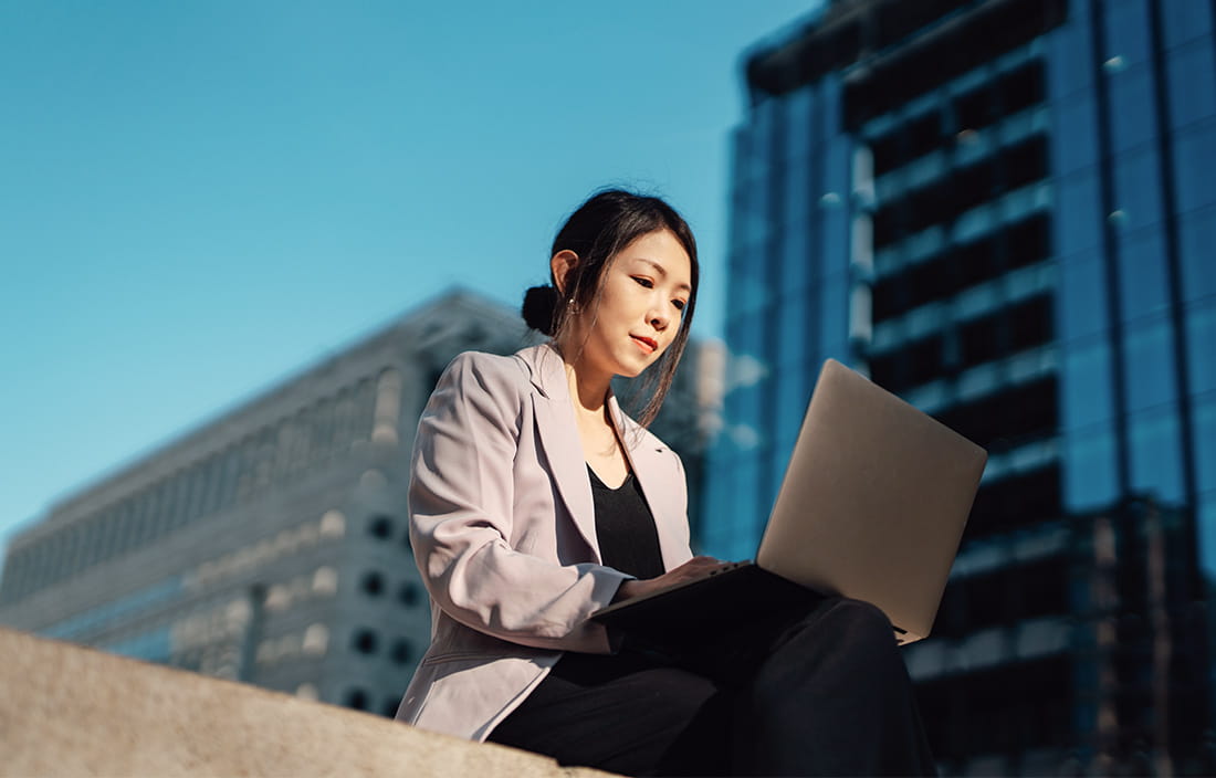 Businesswoman comparing real estate investments on her laptop with buildings in the background.