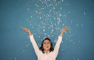 Office woman throwing confetti in the air on a blue background to celebrate award