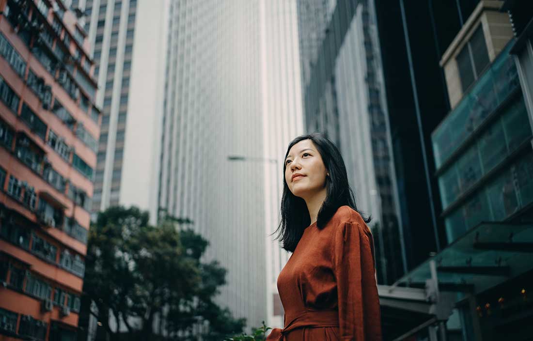 Asian women framed by tall city buildings thinking about refinancing her commercial building to unlock liquidity in her business