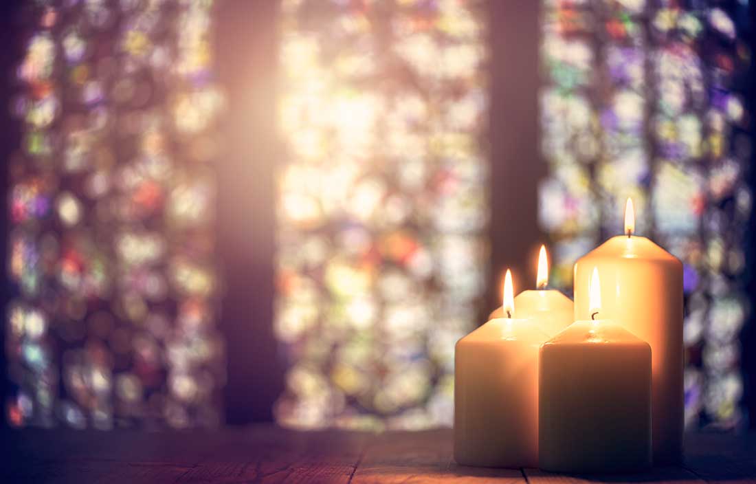 Three candles in a church with stained glass in the background