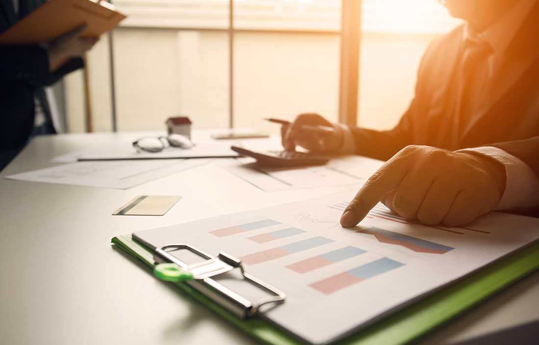 Two real estate consulting professionals at a table reviewing tables and graphs showing rent collections for their client's owned commercial real estate properties.