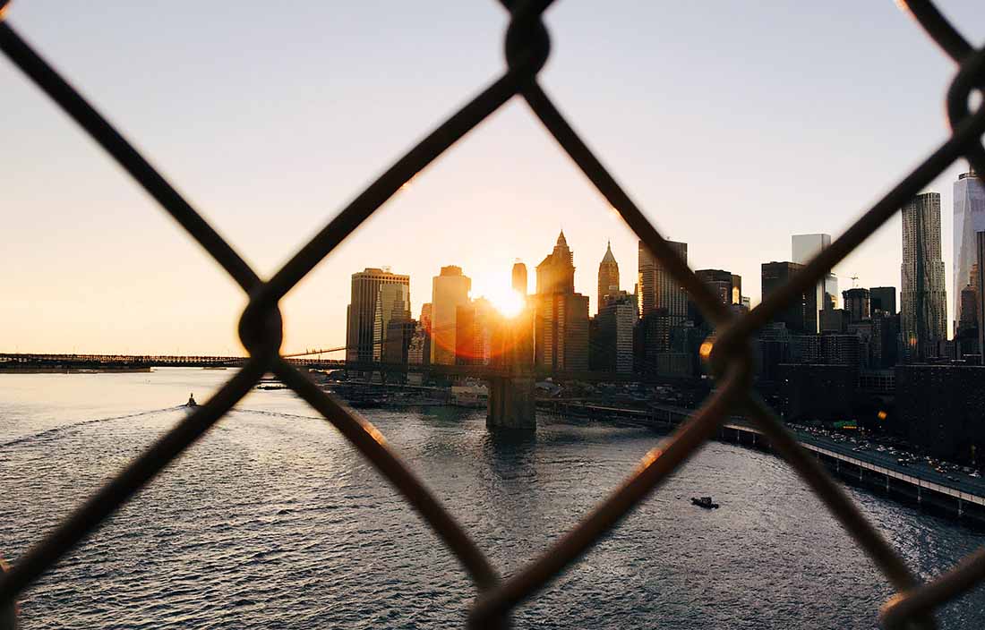 Image of the New York harbor at sunset through a chain link fence