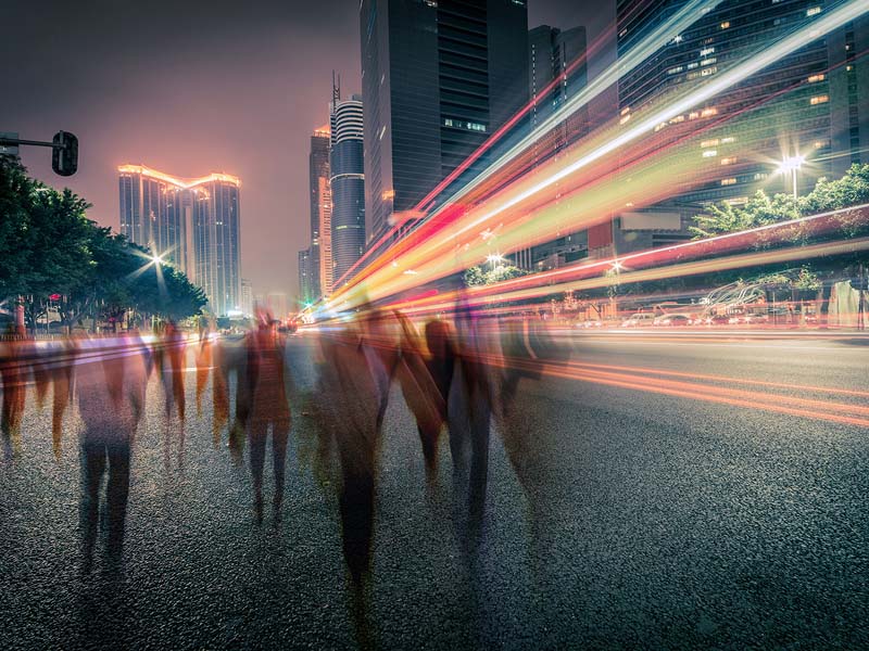 City street with buildings behind a streak of lights and shadowy figures