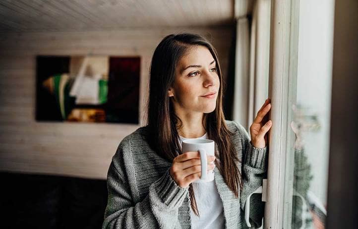 Woman holding a mug and looking out a window.