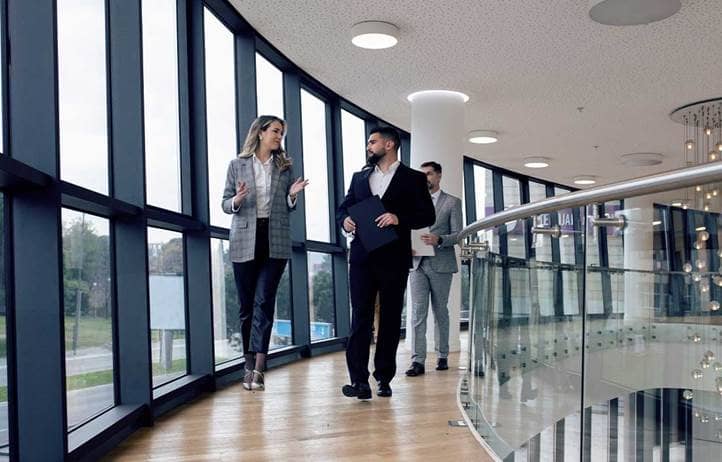 Man and woman walking in an office hallway and talking to each other.
