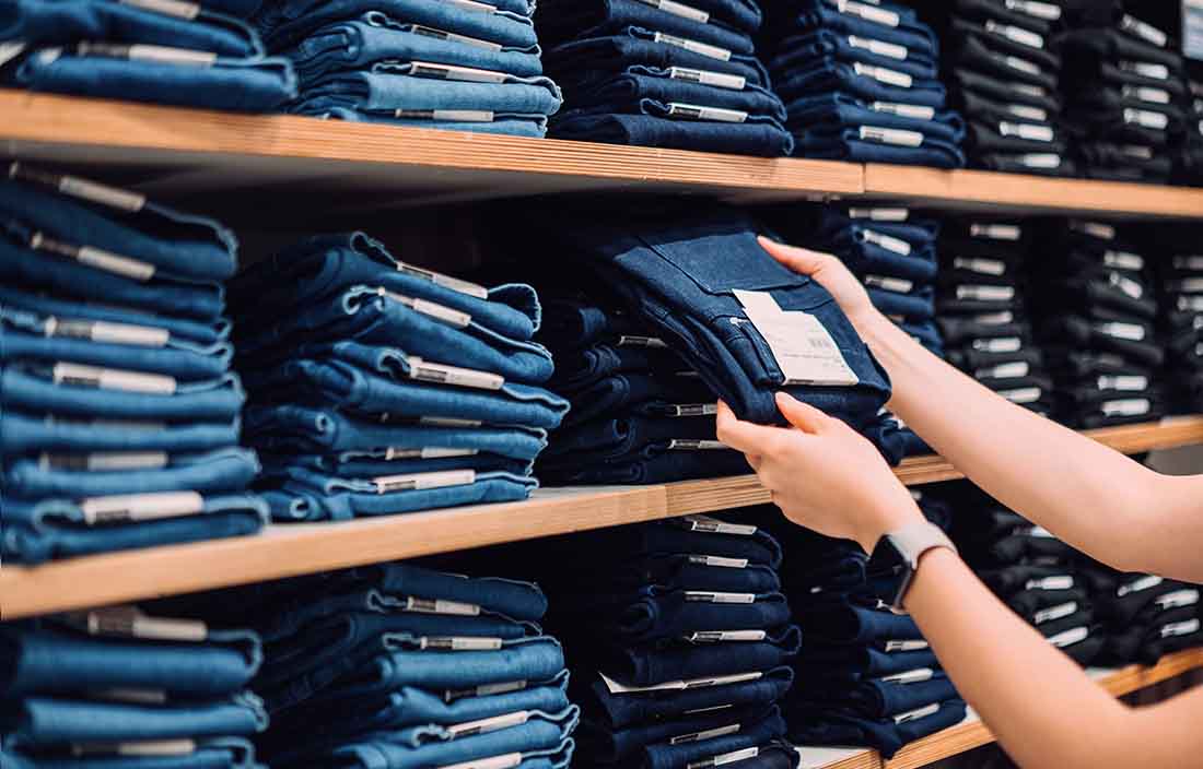 Shelf full of jeans with person putting a pair back