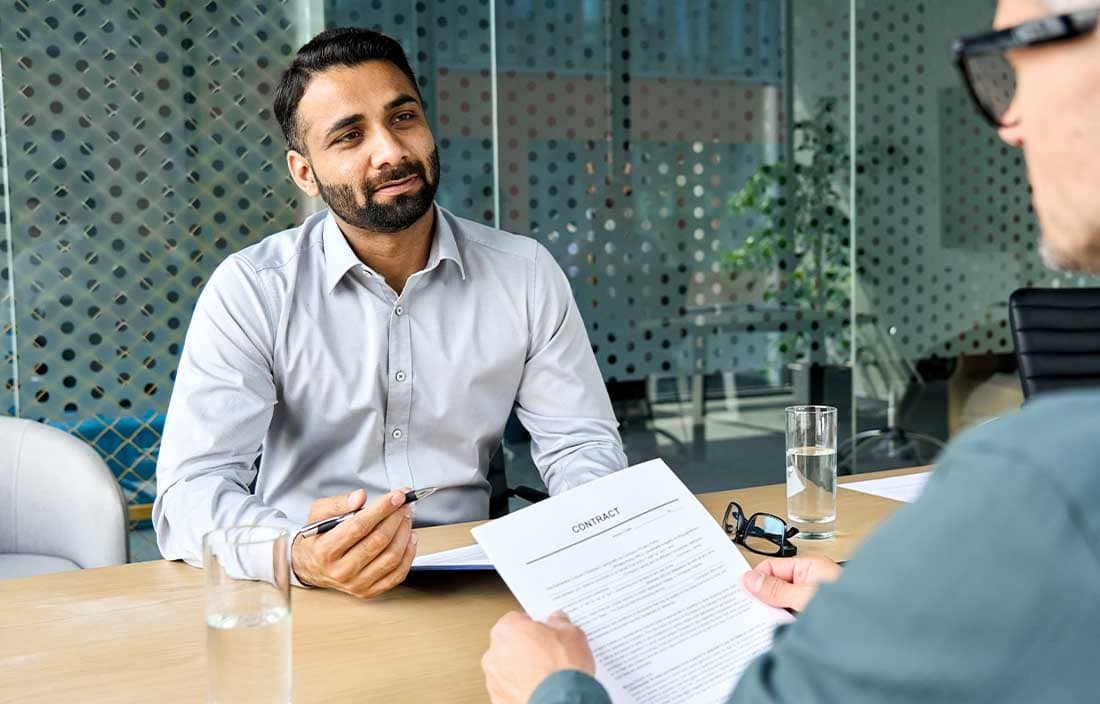 Man looking across the table to another man holding a job contract.