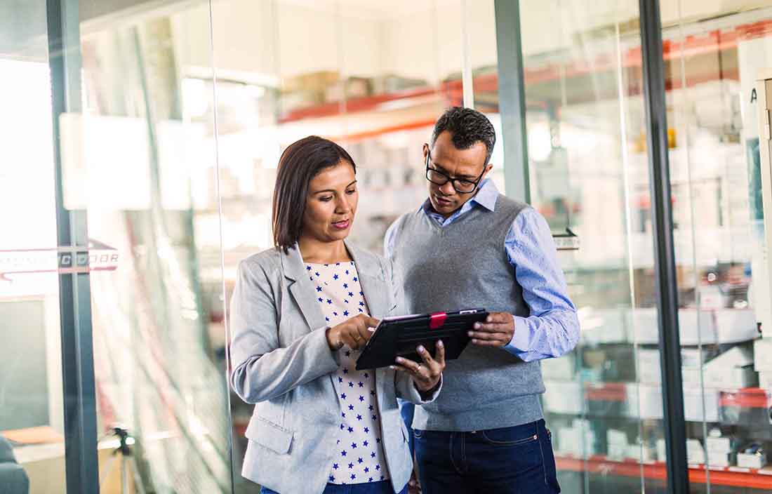 Two people standing in an office looking at a tablet
