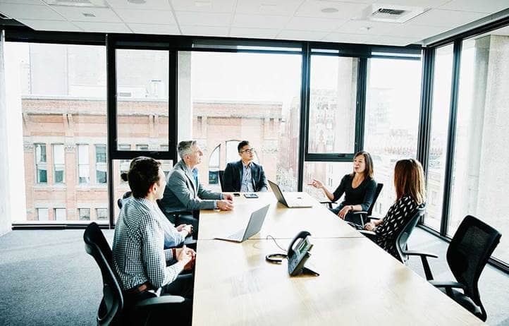 Group of people talking to each other a long table in an office. 