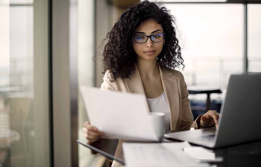 Woman holding a paper and looking at computer