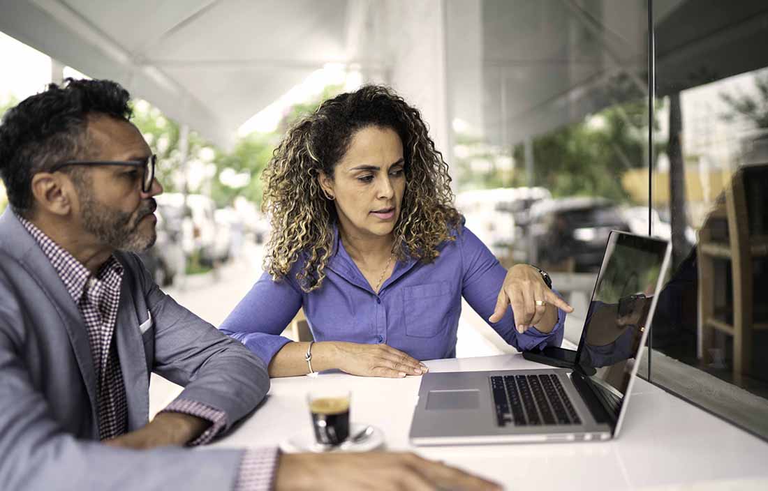 Two people sitting at table outside looking at computer