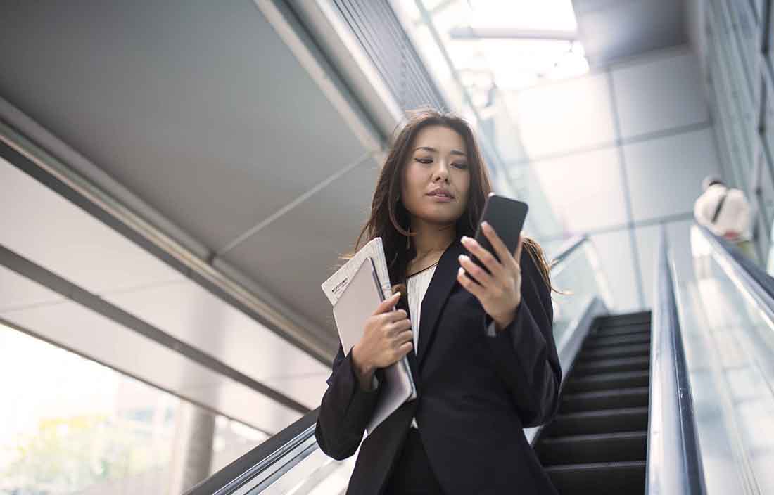 Person walking down the stairs looking at phone and holding papers