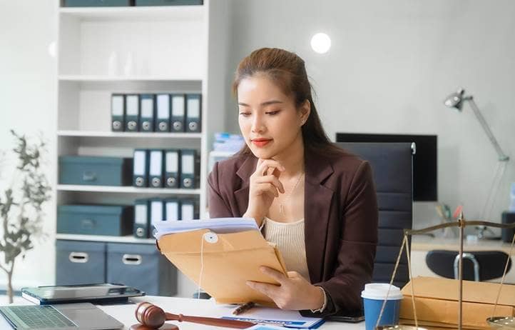 Women in a blazer at a desk looking down at a piece of paper.