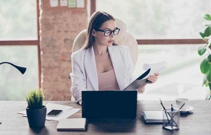 Women at a desk with a computer open looking at a clipboard.