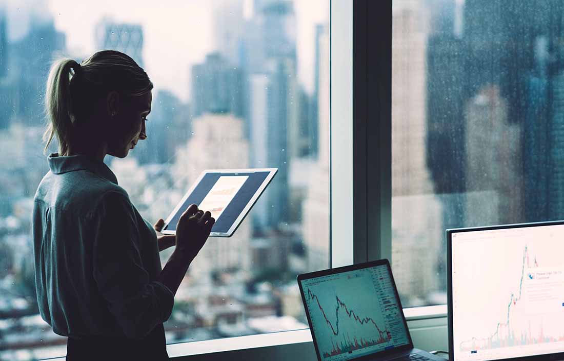 Woman standing in office looking at equity performance on a tablet