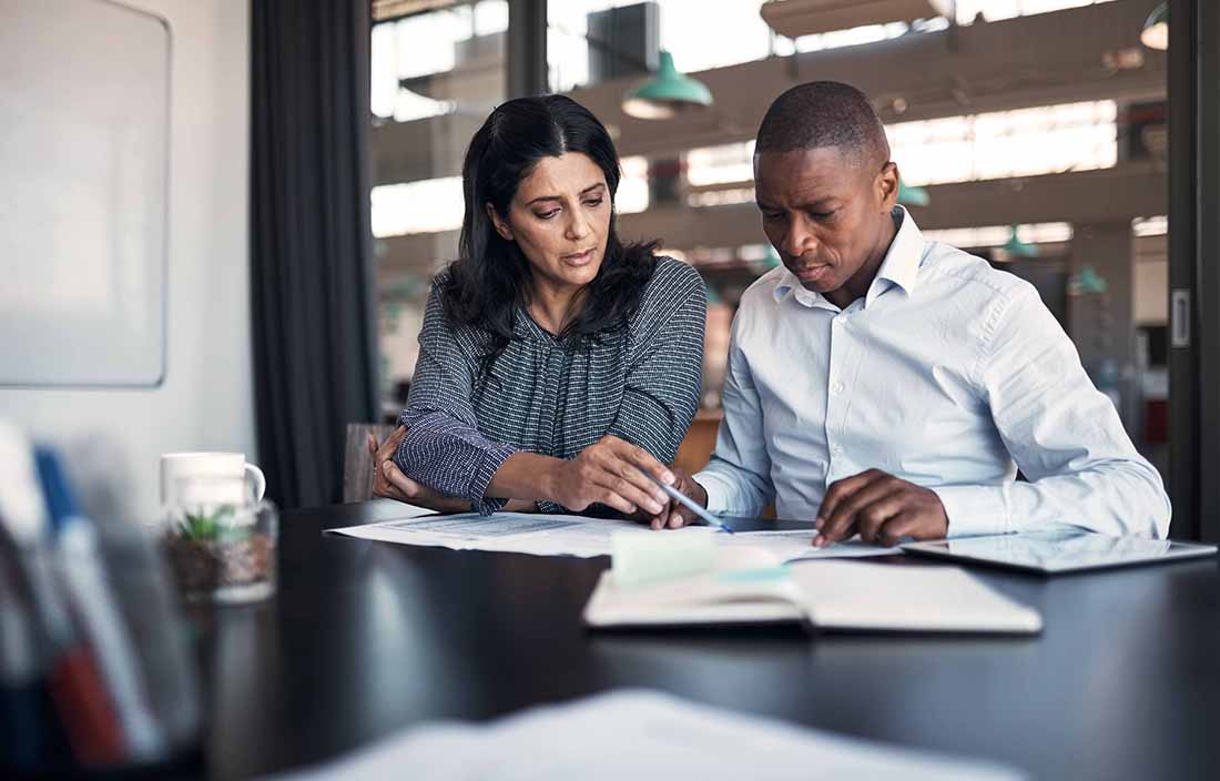 Two people sitting in a room looking at papers and discussing a diverse portfolio