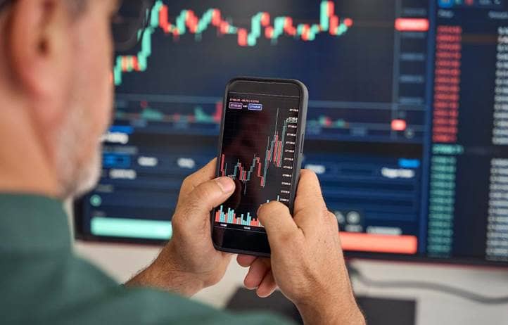 Man looking at charts on phone and computer