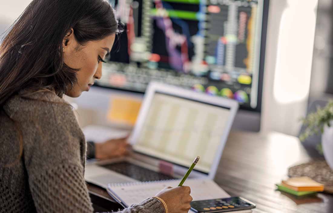 Woman sitting at her computer looking at economic data and calculating potential investment opportunities