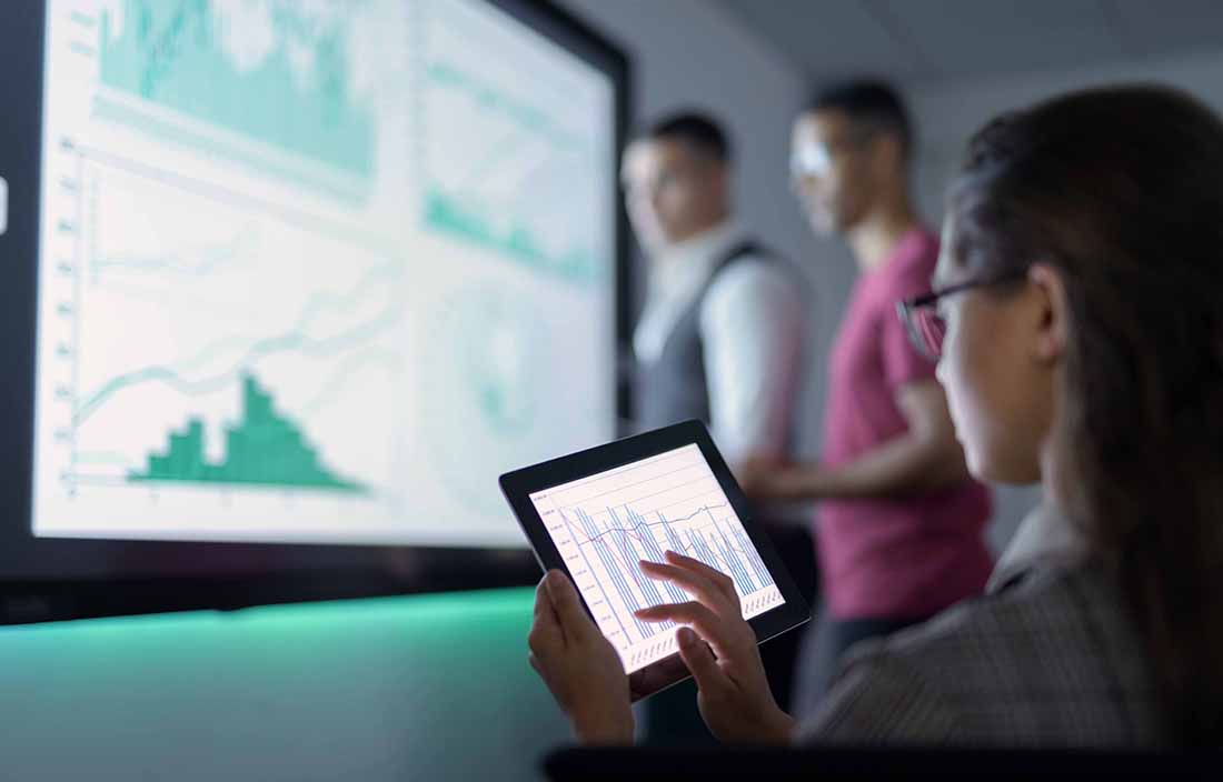 Person looking at credit delinquency data on a tablet with two people in the background looking at other economic data points