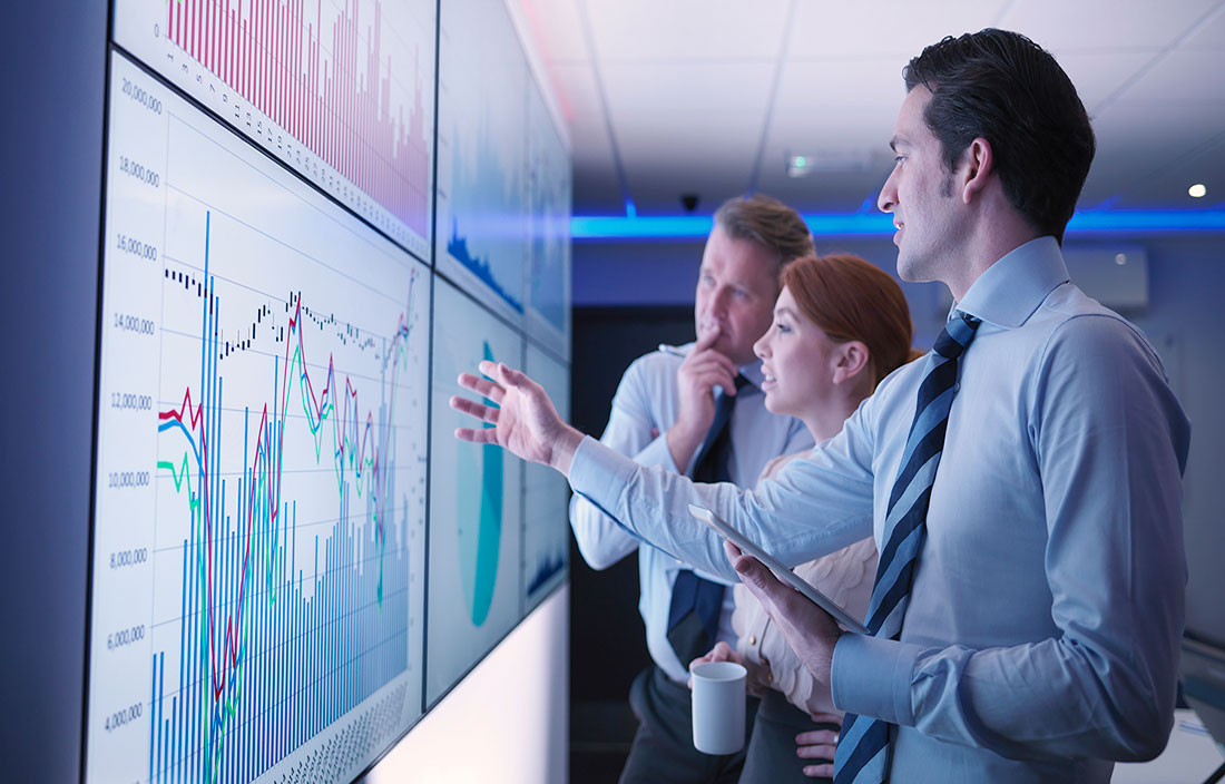 Plante Moran Market Perspectives - Three business people discuss graphs on screen in meeting room