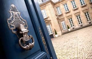 Opened door with a brass dorr knocker with view of a historic building.