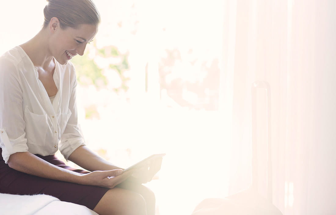 Woman sitting and looking downward at a tablet, smiling.