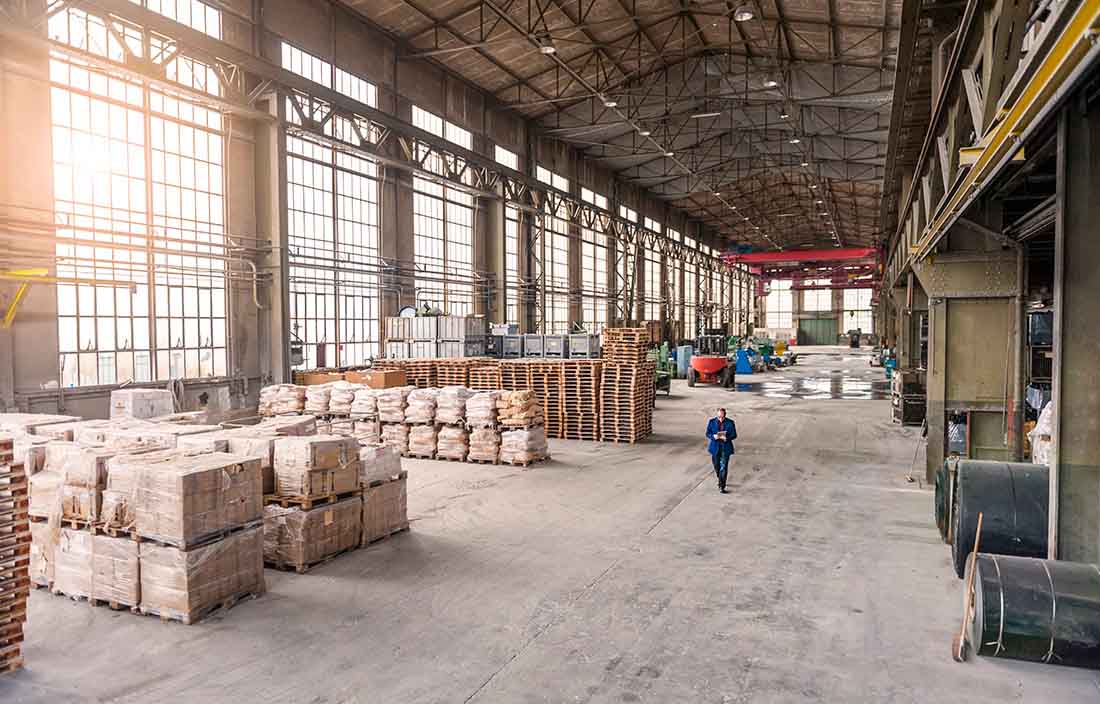 Warehouse worker walking through a big warehouse with shelving units and loading docks.