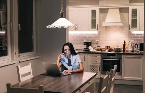 Young woman sitting at dining room table browsing on her laptop computer.
