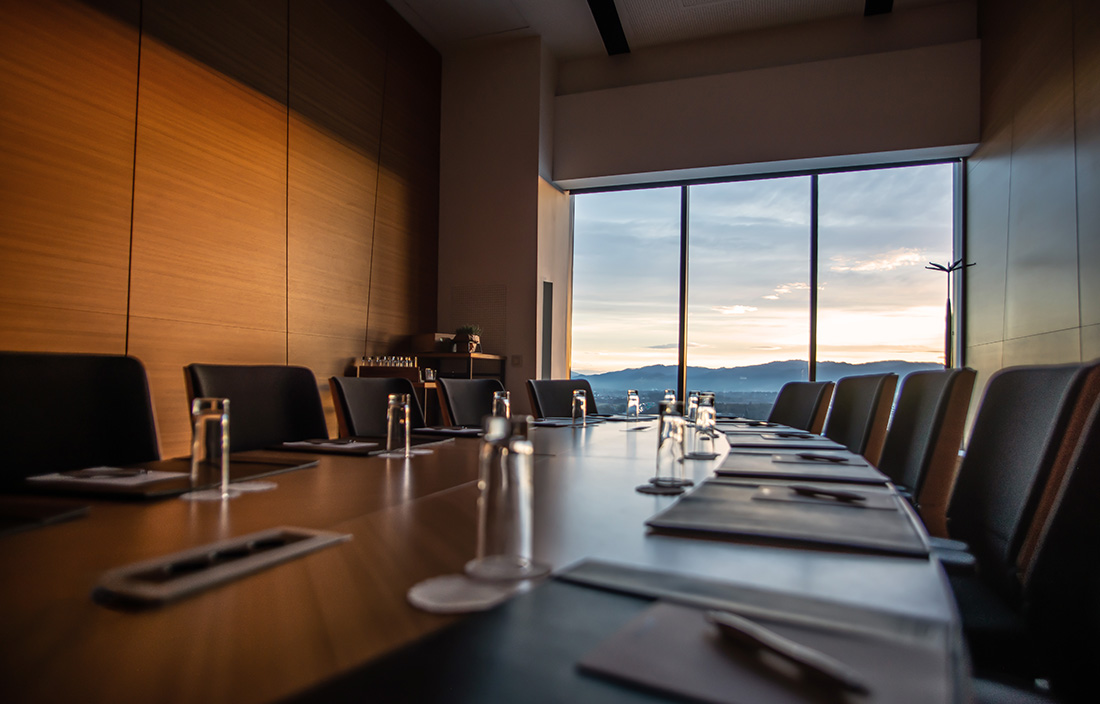 Close-up photo of a conference room desk with a view of a sunrise outside the window in the background.