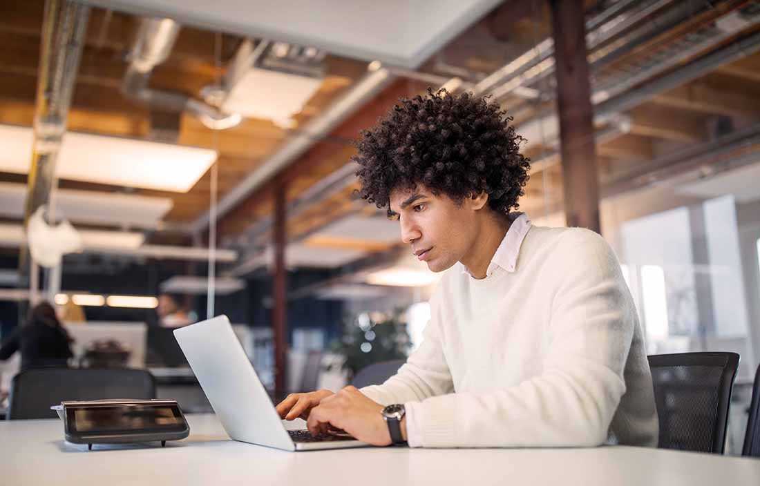 Young business professional sitting at a work table using a laptop computer.