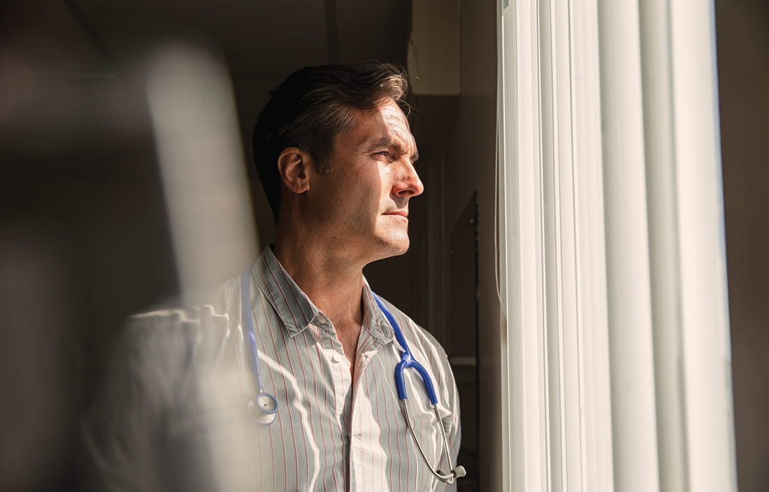 Man wearing a stethoscope while looking out a window.