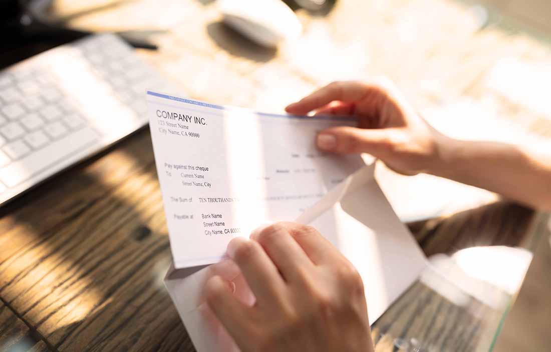 Close-up photo of hands opening a letter and holding a check.