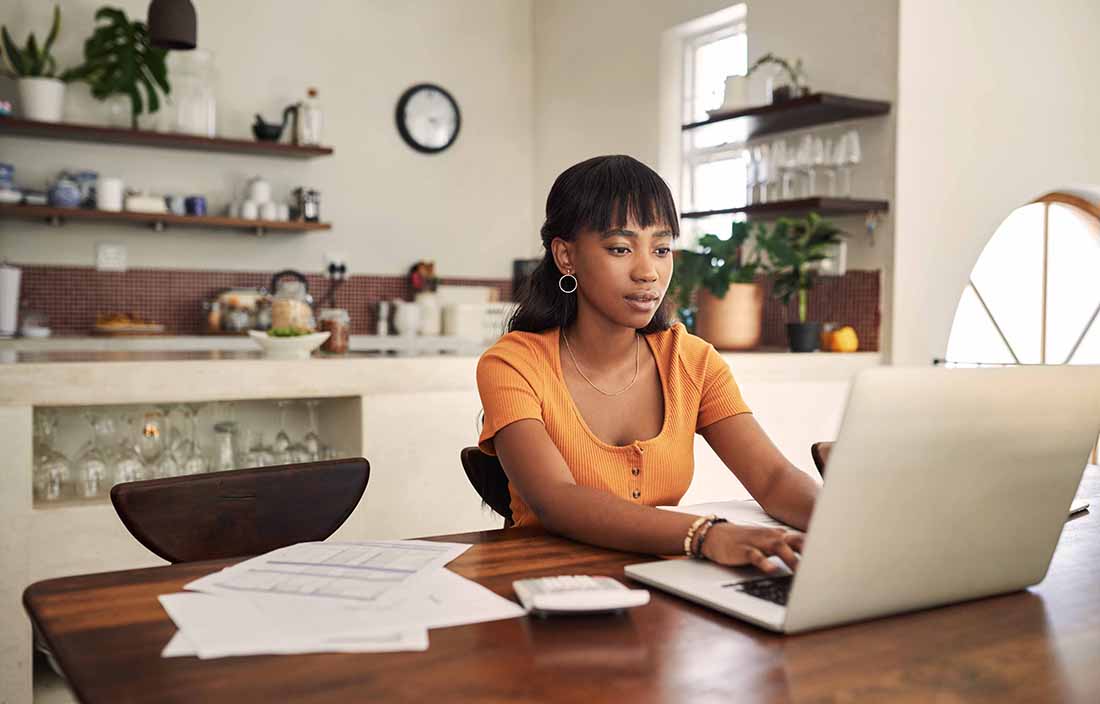 Worker using laptop computer at kitchen table in home office space.