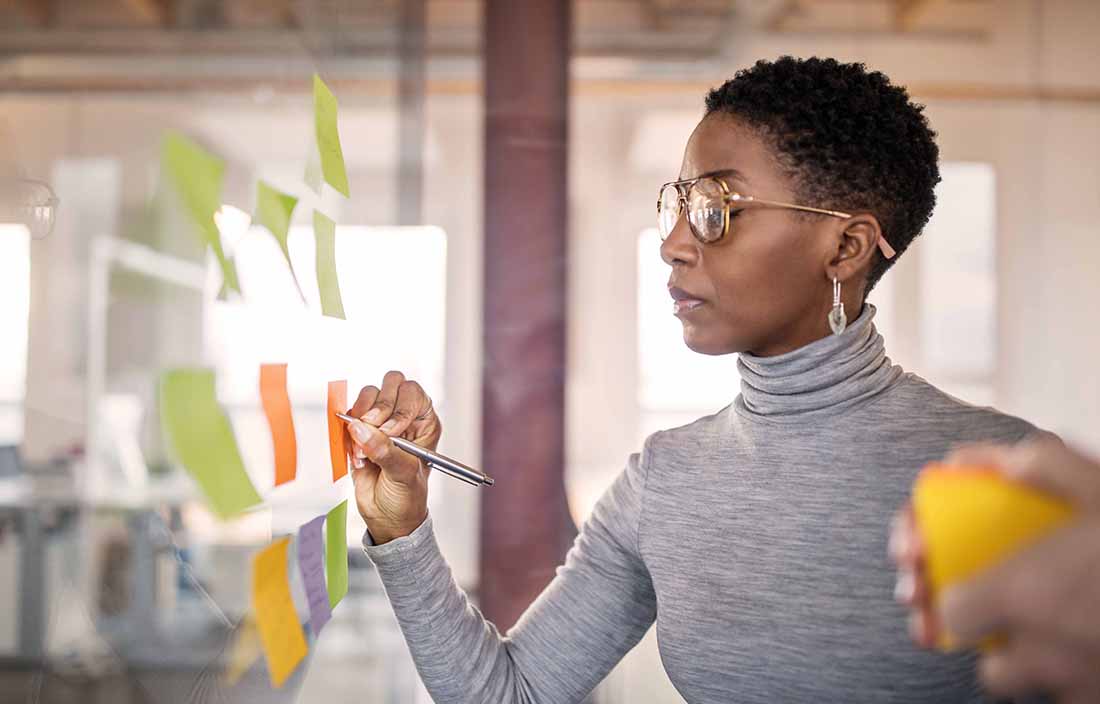 Young business woman writing on post-it notes stuck to a glass window.