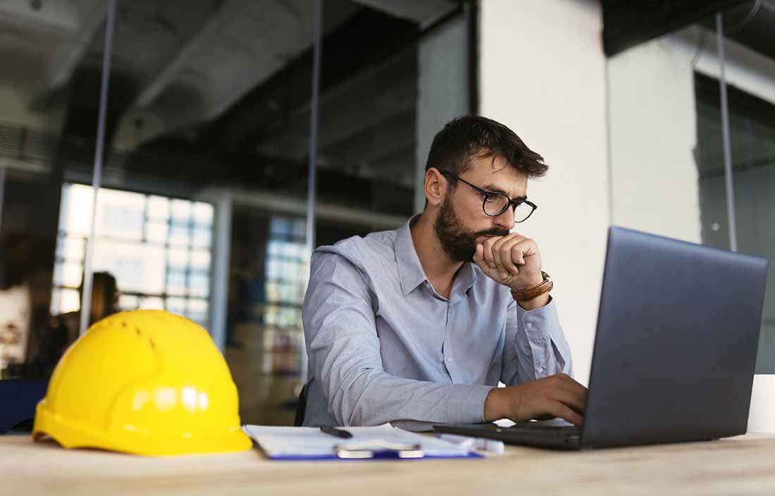 Construction foreman sitting at a table using a laptop computer.