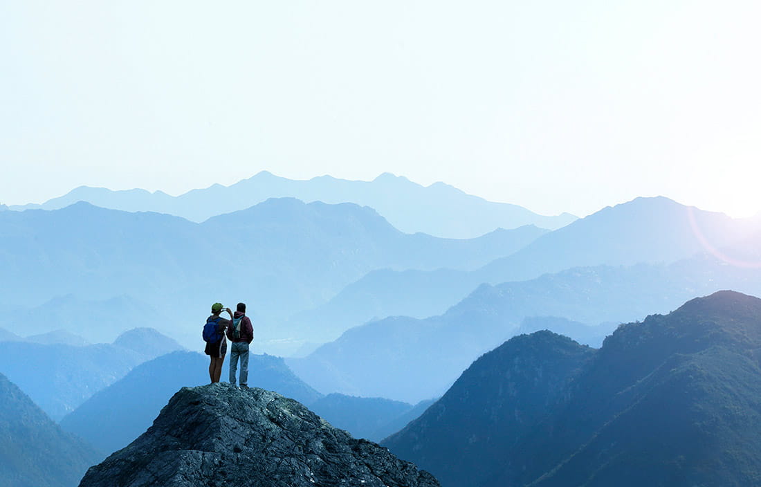 Two hikers on a mountain taking a photo of the view.