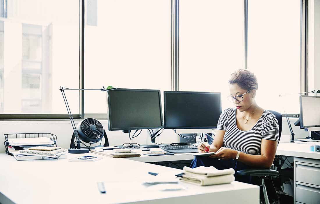 Businesswoman sitting at her desk taking notes on a notepad.