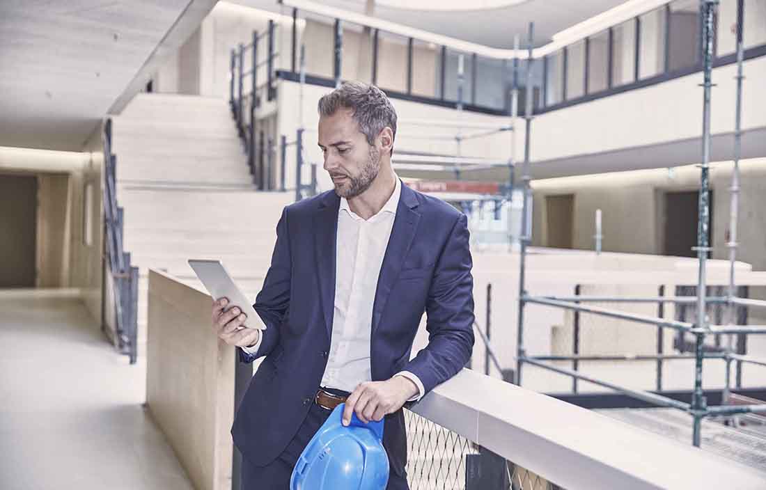 Businessman leaning against a railing in a lobby area using his cell phone.