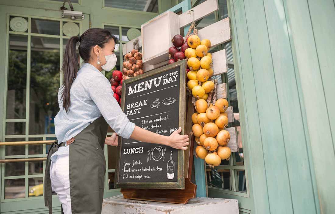 A food worker setting up a menu sign in an outdoor area.