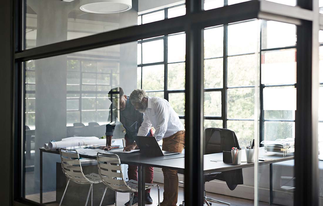 Two businesspeople in a conference room leaning over a desk reviewing notes.