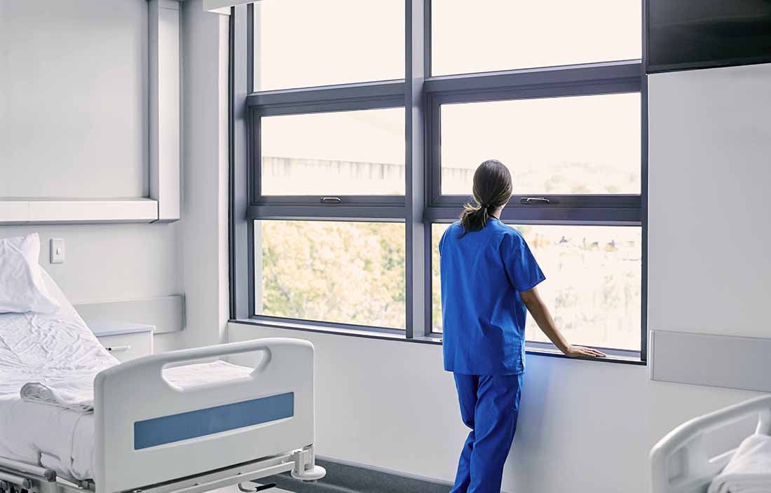 Nurse standing at hospital room window looking out the window.