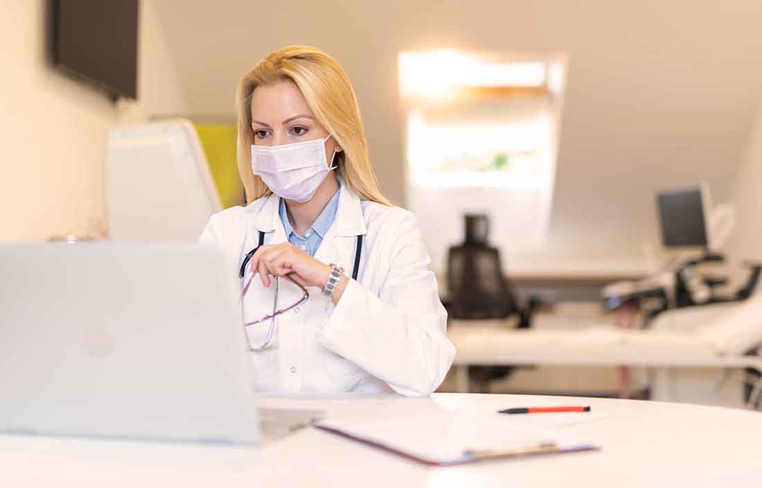 Doctor using a laptop computer while wearing a protective facemask.