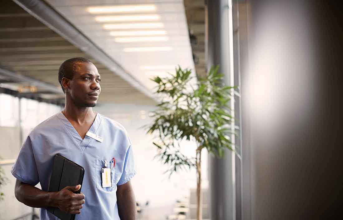 Healthcare professional holding a padfolio looking out a window.