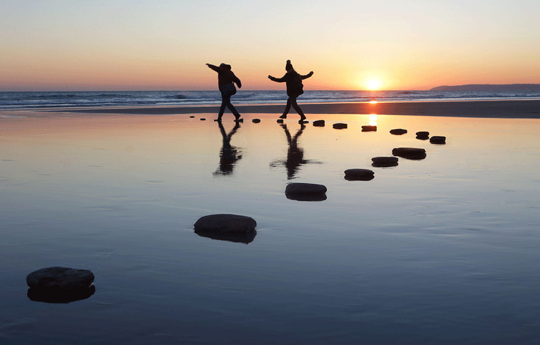 Two people walking on stones in water.