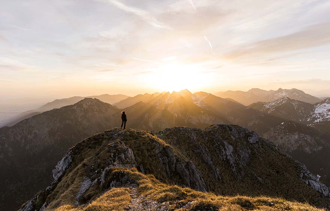 Hiker standing on a mountain looking at a sunset.