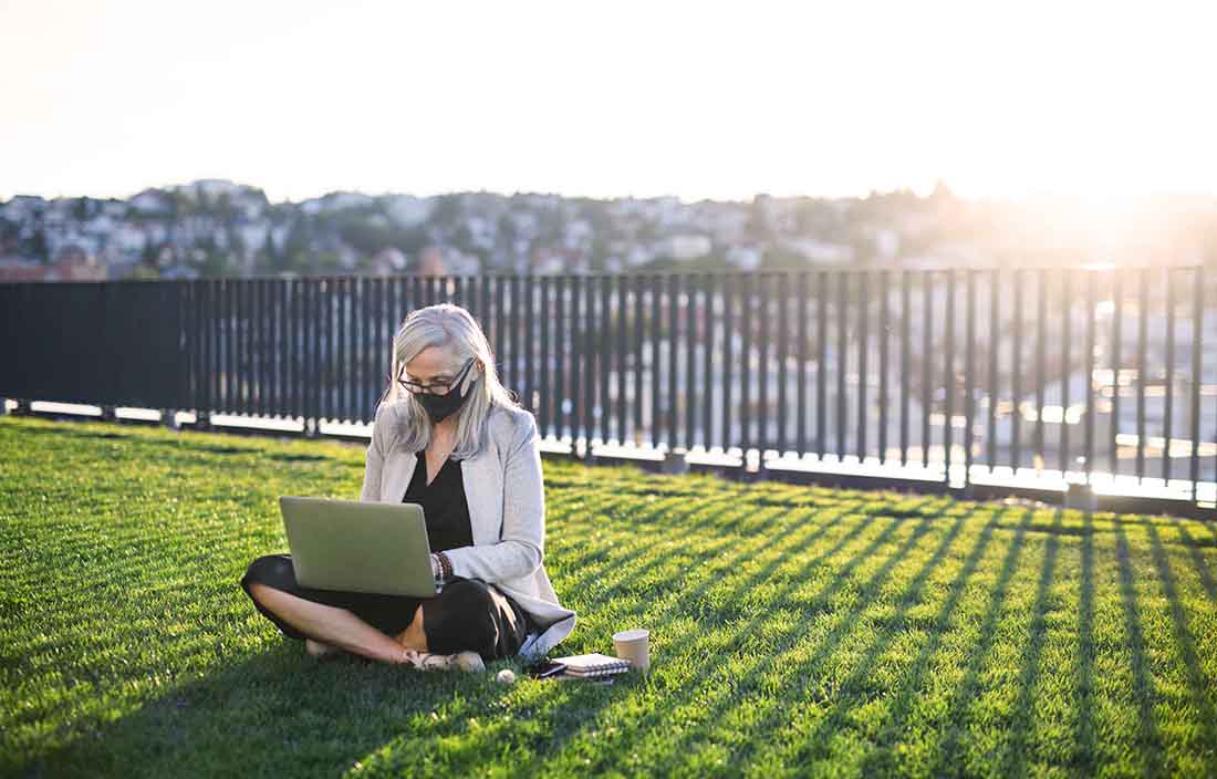 Elderly business professional sitting on grass while using their laptop computer.