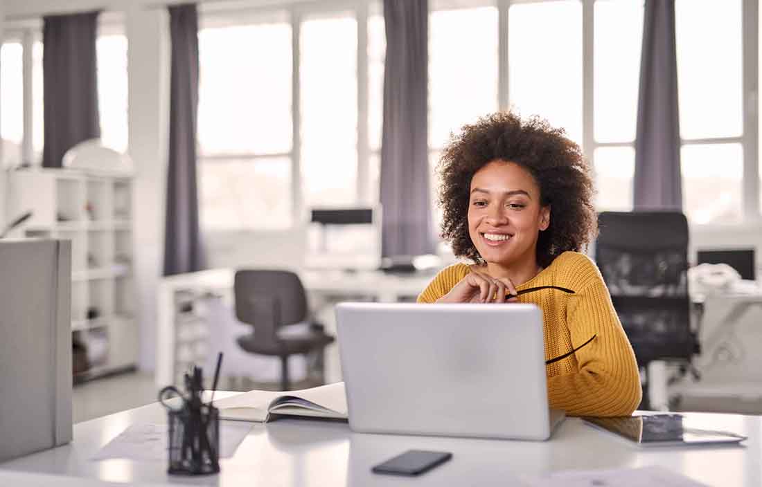 Business professional in a yellow sweater using a laptop computer.