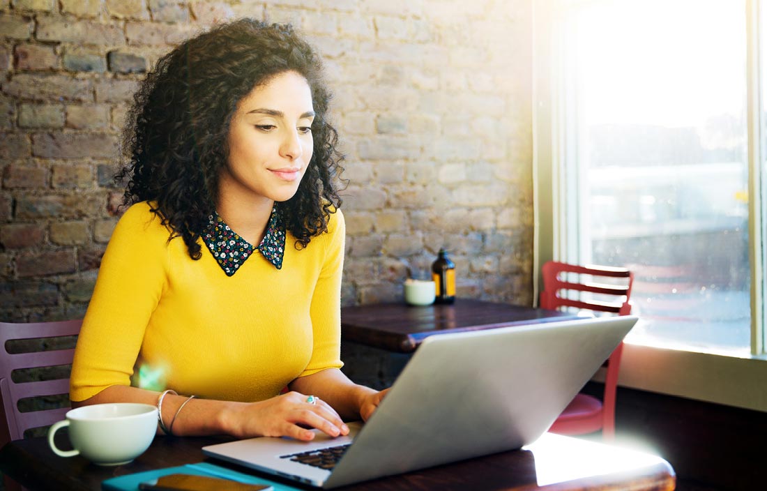 Business professional wearing a yellow sweater sitting at their desk using a laptop computer.